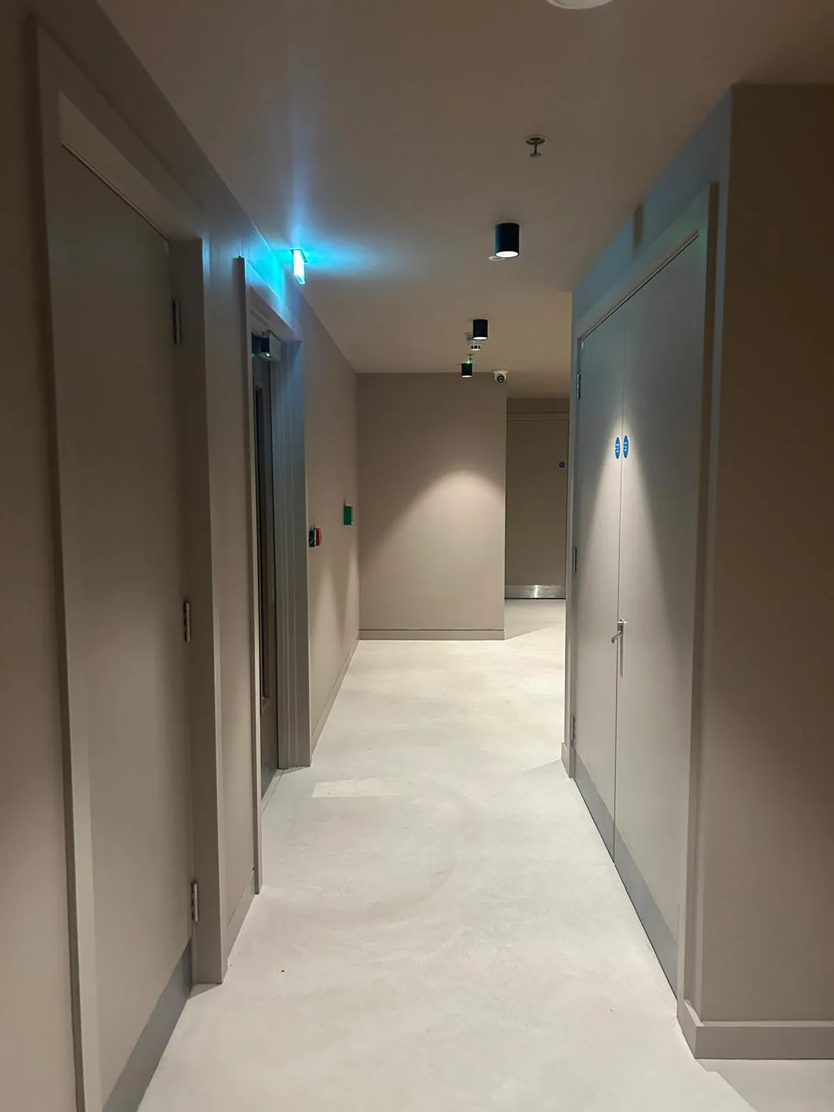 A finished communal corridor with taupe walls and doors, grey skirting and a pale floor